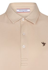T-shirt polo beige en tissu texturé, avec un col, trois boutons et un logo d'oiseau brodé sur la poitrine gauche.