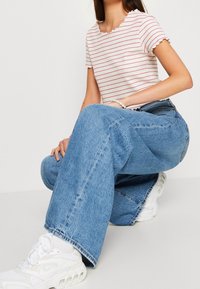 Stripet kortærmet top i hvid og rød; høj talje blå denim brede ben jeans; hvide sneakers med strukturelle detaljer.