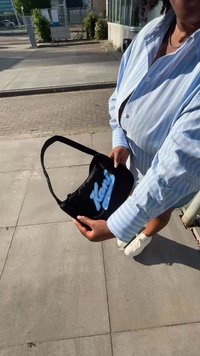 Juodas peties krepšys su mėlynu logotipu "Kani" priekyje, pagamintas iš lygaus medžiagos, plokščios formos ir su vienu reguliuojamu diržu.