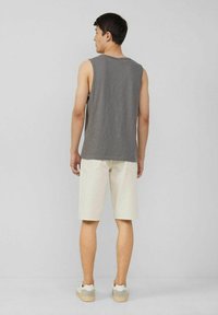 Graues ärmelloses Shirt kombiniert mit hellbeigen Shorts. Die Shorts verfügen über Gesäßtaschen. Das Modell trägt weiße Sneakers. Schlichte und entspannte Passform.