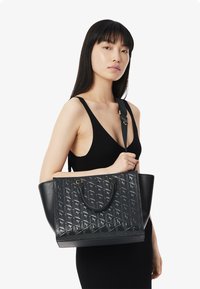 Borsa a tracolla nera con un motivo geometrico testurizzato, doppi manici e tracolla regolabile. Realizzata in pelle liscia e resistente.