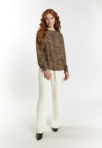 Long-sleeve brown blouse with a cream abstract pattern, paired with cream wide-leg pants and brown heeled shoes on a plain background.