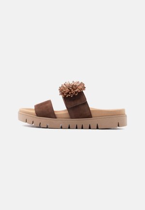 Brown slip-on sandal with two suede straps, a floral embellishment on the upper strap, and a thick ridged beige sole.