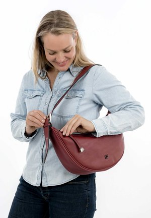 Sac à bandoulière en cuir rouge avec une forme courbée, doté d'une fermeture éclair et d'un logo décoratif. Design léger avec une large sangle.