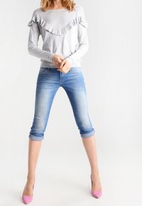 Šedý dlouhý rukáv s volánkovým límcem, zkombinovaný s bledě modrými zkrácenými džíny a růžovými vysokými podpatky. Džíny mají minimální opotřebení.