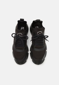 Svarta stickade sneakers med texturerad ovandel, gummidetaljer och platta snören. Inkluderar branding på tungan och sidan. Rundad form.