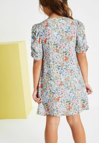 Vaaleansininen kukkamekko lyhyillä puffihihnoilla, jossa on monivärisiä niittykukkakuvioita ja liehuva helma.