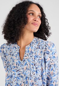 Blauw en roze gebloemde blouse met een v-hals, geplooid ontwerp en knoopdetails. Gemaakt van lichtgewicht stof met een soepele textuur.