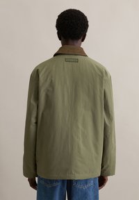 Kurtka khaki z brązowym kołnierzem z sztruksu, o luźnym kroju i tylną metką marki. Materiał wydaje się gładki i lekki.