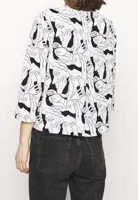 Blusa a maniche corte con un motivo astratto di volti in bianco e nero, realizzata in tessuto leggero, con una vestibilità rilassata e scollatura rotonda.