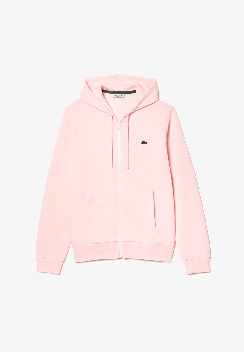 Sweat à capuche zippé rose clair avec poches frontales, cordons et petit logo crocodile vert sur la poitrine gauche. Aucune personne présente.