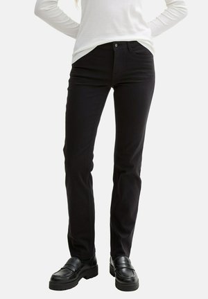 Pantalones negros de mezclilla con corte recto, bolsillos delanteros y cierre de botón. Combinados con mocasines negros, la tela tiene una textura suave.