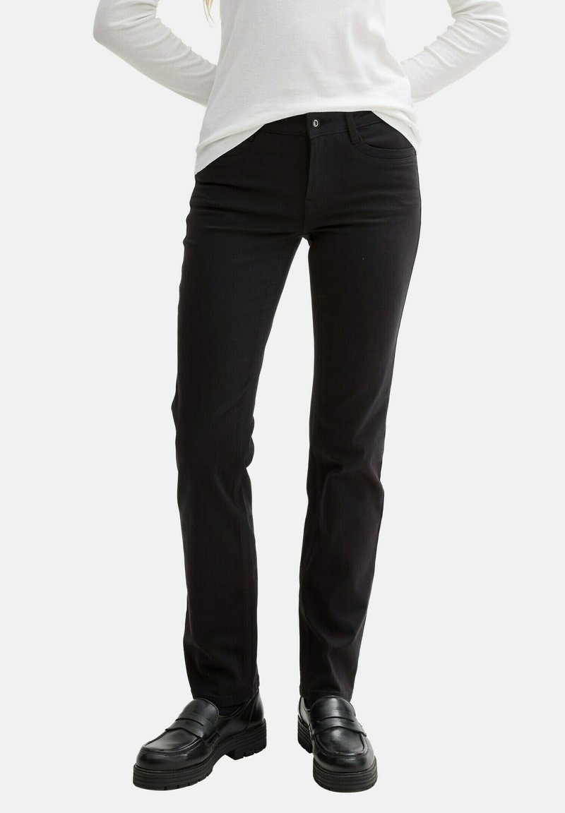 Pantaloni neri in denim con taglio dritto, tasche frontali e chiusura con bottone. Accoppiati con mocassini neri, il tessuto ha una consistenza liscia.