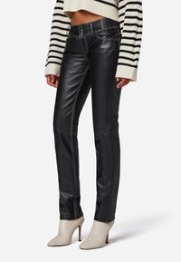 Zwarte leren broek met contrasterende stiksels, slim fit ontwerp en een middelhoge taille, gecombineerd met lichtgekleurde enkellaarsjes met hak.