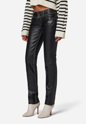 Zwarte leren broek met contrasterende stiksels, slim fit ontwerp en een middelhoge taille, gecombineerd met lichtgekleurde enkellaarsjes met hak.