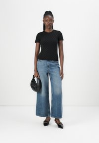 Black knitted short-sleeve top with dot pattern, paired with light blue wide-leg jeans. Model holds a small black handbag and wears black heels.