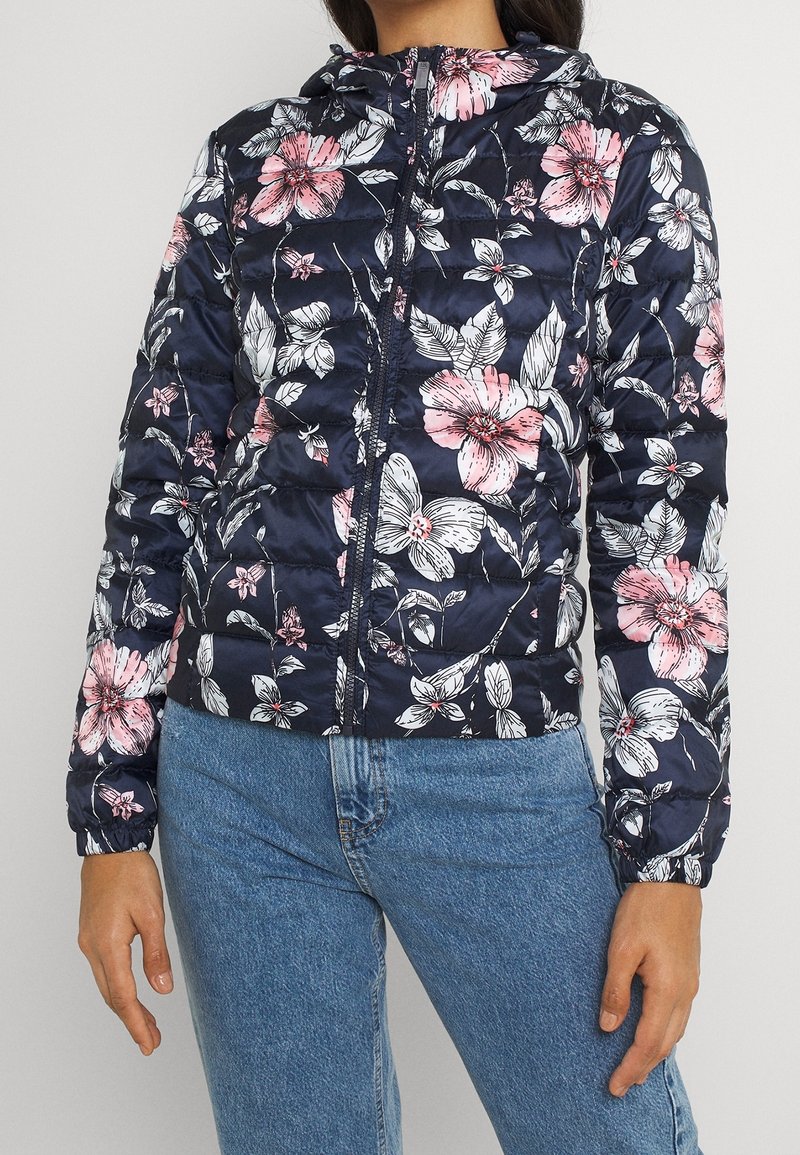 Veste matelassée bleu marine avec un motif floral comprenant des fleurs roses et blanches, fermeture éclair complète et capuche, fabriquée en tissu brillant avec un design matelassé.
