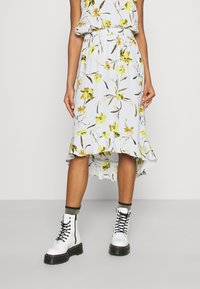 Floraler Midirock in Hellblau mit gelben und grünen Blumenmustern, elastischem Bund und einem gerafften Saum. Kombiniert mit weißen Combat-Stiefeln.