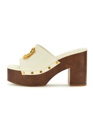 Sandalia plana blanca con tacón cuadrado marrón, detalle de hardware dorado y studded decorativos dorados a lo largo de la suela. Acabado suave.