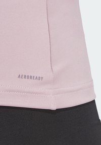 Un primo piano di un abbigliamento sportivo di tessuto viola chiaro con cuciture visibili e il testo "AEROREADY" sopra un tessuto nero.