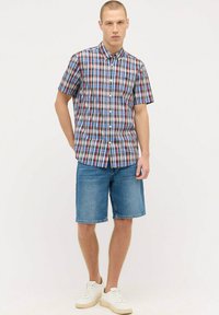 Kurzarm, karierter Hemd in Blau, Rot und Weiß mit einem Button-Down-Kragen; kombiniert mit blauen Denim-Shorts und weißen Sneakern.
