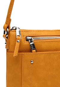 Bolso de cuero amarillo con un acabado texturizado, herrajes plateados, bolsillo con cremallera y correa ajustable. Nota el diseño en capas y la costura.