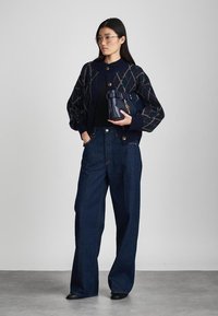 Cárdigan de punto azul marino con patrón geométrico, combinado con unos vaqueros de pierna ancha de mezclilla oscura de cintura alta. Lleva un bolso de piel azul marino.