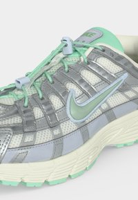 Αθλητικό παπούτσι Nike με ασημένιες επικάλυψεις, δίκτυο σε πράσινο μέντας, λογότυπο Swoosh σε πράσινο μέντας και σύστημα γρήγορου δέσιμου σε λευκή σόλα με υφή πάτου.