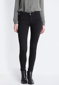 Svarta smala jeans med en slät yta, hög midja och diskreta framfickor, i kombination med en grå skjorta med knappar och svarta ankelskängor.