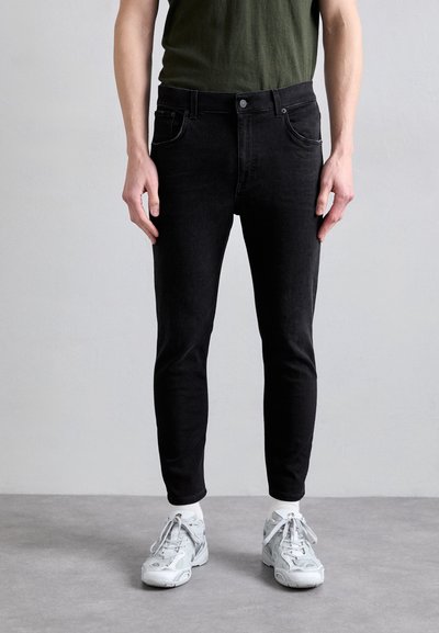 Černé džíny z denimu se slim fit, středním pasem a decentním prošíváním. Spárovány se světle šedými teniskami a zeleným tričkem.