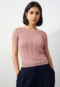 Lyserød strikket kortærmet top med mønstret tekstur og ribbet kant, kombineret med marineblå højtaljede bukser.