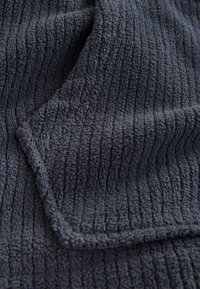 Tissu texturé gris foncé avec des lignes verticales en relief et un coin plié montrant le matériau doux et épais.
