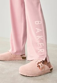 Světle růžové semipánkové pantofle s měděným sponou. Doprovodné růžové tepláky zdobí slovo "BAKER" v tučném, světlém písmu.