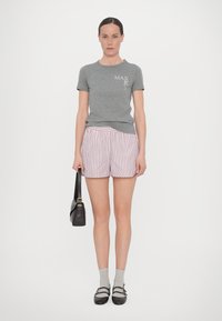 Camiseta de algodón gris con texto blanco, combinada con shorts a rayas rosas y blancos. Un bolso negro de hombro y calcetines grises con zapatos negros completan el atuendo.