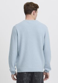 Svetlo modra pulover s krožnim ovratnikom in rebrastimi manšetami, izdelan iz mehke, teksturirane tkanine. Enostavna zasnova brez vzorcev ali poudarkov.