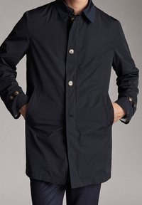 Navy blue coat featuring a button closure, pointed collar, and two front pockets; crafted from smooth, lightweight fabric with a streamlined design.