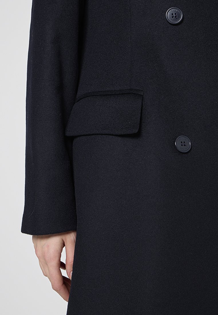 Donker wollen jas met een enkele borstzak en twee knopen aan de voorkant. De stof heeft een zachte textuur en een getailleerde pasvorm.