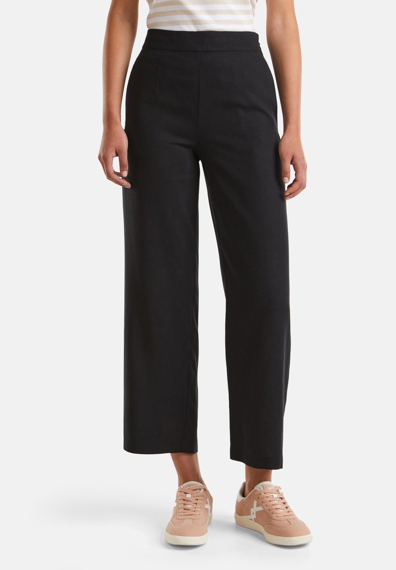 Schwarze weite Hosen aus einem glatten Stoff mit hoher Taille. Kombiniere sie mit hellrosa Sneakers mit weißen Akzenten.