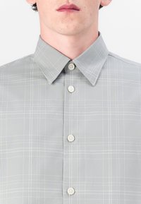Lys grå skjorte med knapper og rutete mønster, med små knapper, en myk krage og en glatt tekstur.