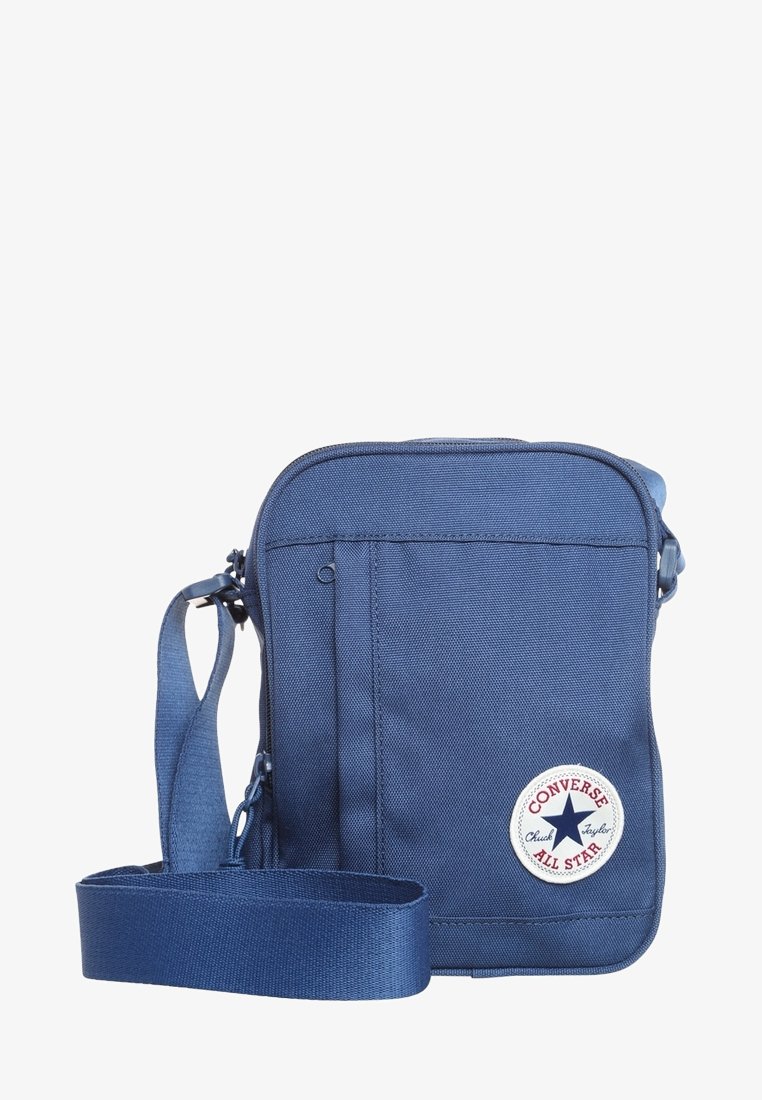 Sac bandoulière bleu Converse All Star avec une bandoulière réglable, des compartiments zippés et un écusson rond portant le logo, sur fond blanc.