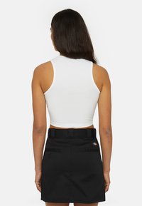 Witte cropped tanktop met een hoge halslijn, gecombineerd met een zwarte rok met ceintuurlussen en zakken. Glad materiaal en een aansluitend ontwerp.