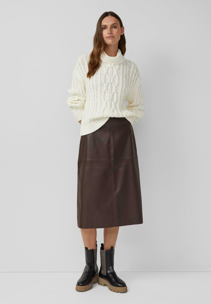 Pull en tricot crème avec un motif en câble, associé à une jupe midi en cuir marron. Bottines noires avec des semelles épaisses et des accents texturés.