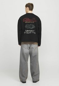 Felpa nera oversize con grafiche rosse e verdi sul retro, abbinata a pantaloni in denim grigi larghi. Texture liscia.