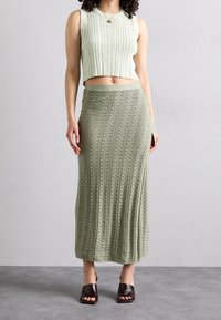 Lichtgroene geribbelde crop top en een lange, gestructureerde rok in een bijpassende kleur, gecombineerd met bruine hakken. De rok heeft een gedetailleerd patroon.