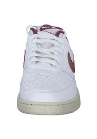 Sneaker in pelle bianca con logo Nike rosso, punta rotonda, dettagli perforati e suola piatta in gomma bianca. Presenta un classico design con lacci.