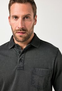 Polo shirt grigio scuro con colletto, tre bottoni e taschino sul petto. Realizzato in un tessuto testurizzato con un motivo sottile.