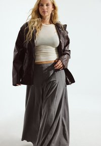 Braune Lederjacke, hellbeige tailliertes Oberteil, lockere graue plissierte Hose, weiche Texturen, minimalistisches Design, heller Hintergrund.