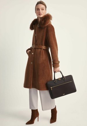 Brązowy wełniany płaszcz z futrzanym kołnierzem, z paskiem w talii, w połączeniu z beżowymi botkami na wysokim obcasie i trzymany czarny skórzany torebkę z złotym zamkiem.