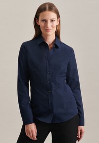 Camicia blu navy con colletto, maniche lunghe e una vestibilità aderente. Tessuto in cotone morbido, con un piccolo logo del marchio sul lato sinistro.