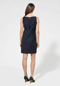 Granatowa, dopasowana sukienka z okrągłym dekoltem z tyłu i detalami w postaci guzików. Gładka faktura, długość do kolan, w połączeniu z czarnymi czółenkami na szpilkach.